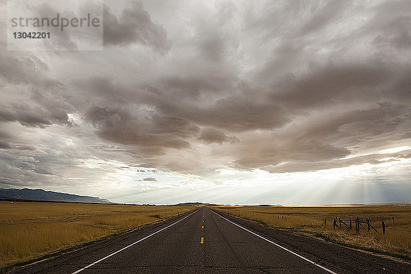 Einspurige Straße mitten auf dem Feld gegen Gewitterwolken