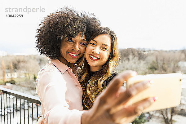 Fröhliche Geschäftsfrauen nehmen sich mit Smartphone auf dem Hotelbalkon ein