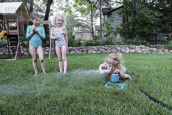 Freunde schauen einem Mädchen zu  das Wasser aus einem Sprinkler auf einem Spielplatz trinkt