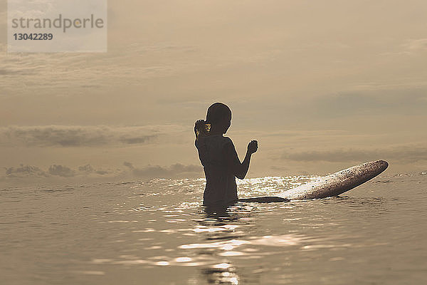 Silhouette einer Frau mit Surfbrett im Meer stehend