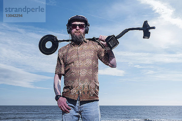 Porträt eines Mannes  der den Metalldetektor am Strand von Horsey Beach gegen den Himmel hält