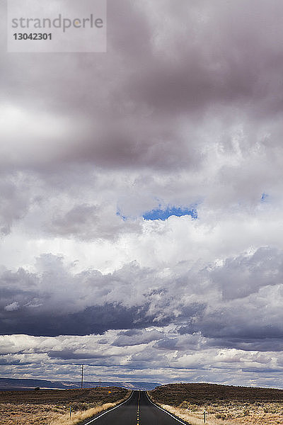 Hochwinkelansicht der Landstraße inmitten des Feldes gegen Gewitterwolken