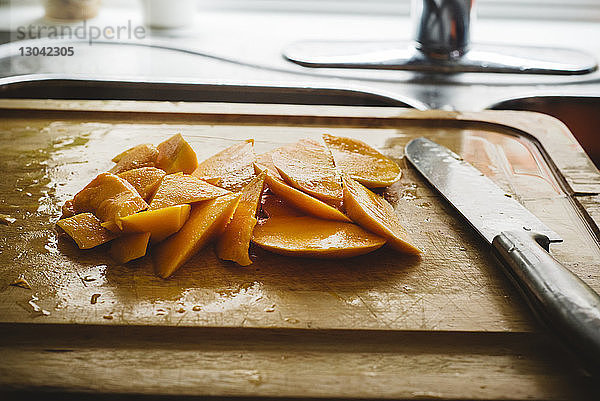 Hochwinkelansicht von Mangoscheiben mit Messer auf Schneidebrett an der Küchenspüle