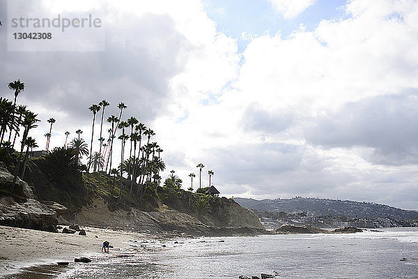 Fernansicht eines Jungen  der am Laguna Beach gegen bewölkten Himmel spielt