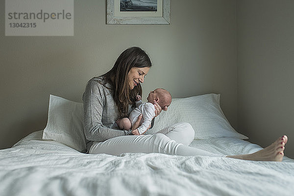 Glückliche Frau in voller Länge spielt mit neugeborenem Jungen zu Hause im Bett
