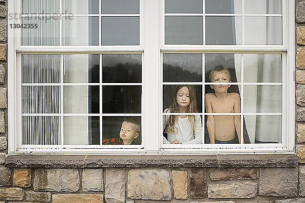 Geschwister schauen zu Hause durchs Fenster