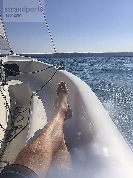 Niedriger Teil des Menschen entspannt sich im Boot auf dem Meer vor klarem Himmel während eines sonnigen Tages