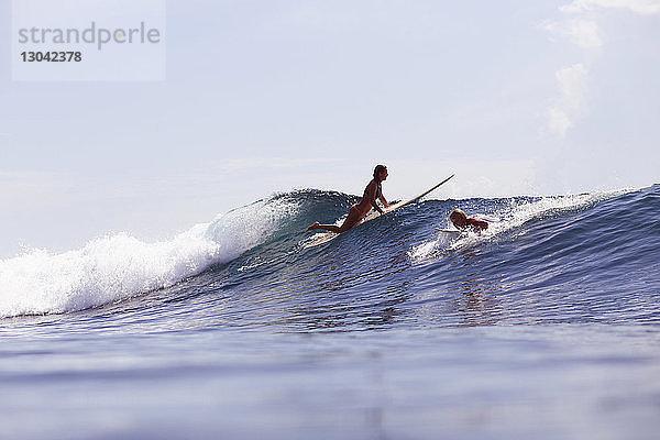 Freunde surfen auf einer Welle im Meer gegen den Himmel