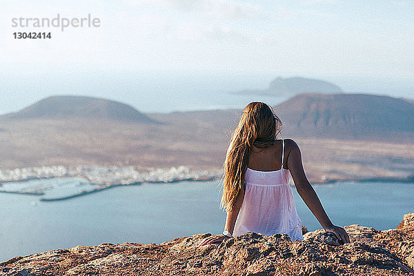 Rückansicht einer Frau  die auf einem Berg gegen eine Insel sitzt
