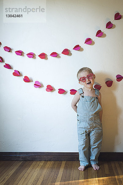 Süßer Junge trägt eine herzförmige Sonnenbrille  während er an der Wand steht