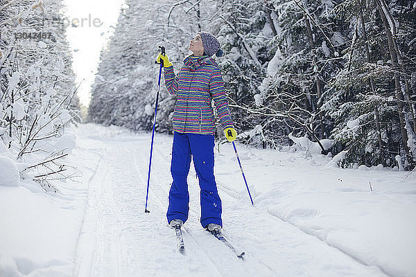 Frau in Skikleidung in voller Länge  die aufschaut  während sie auf einem schneebedeckten Feld steht