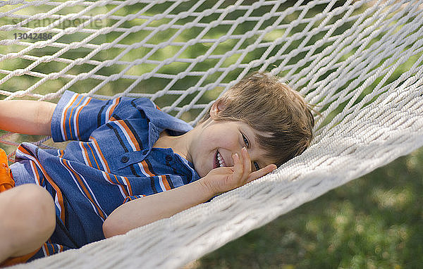 Porträt eines lächelnden Jungen  der auf einer Hängematte im Hof liegt