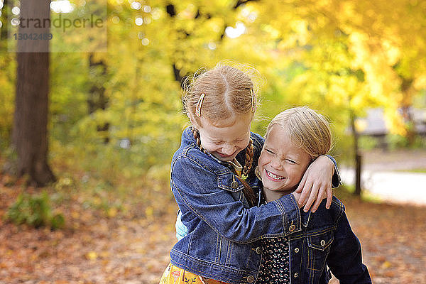 Mädchen umarmt im Herbst fröhliche Schwester gegen Bäume im Hof