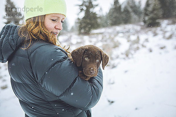 Seitenansicht einer Frau mit Schoko-Labrador auf verschneitem Feld stehend