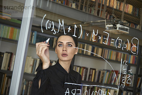 Seriöse Geschäftsfrau schreibt Formel an Glaswand im Büro