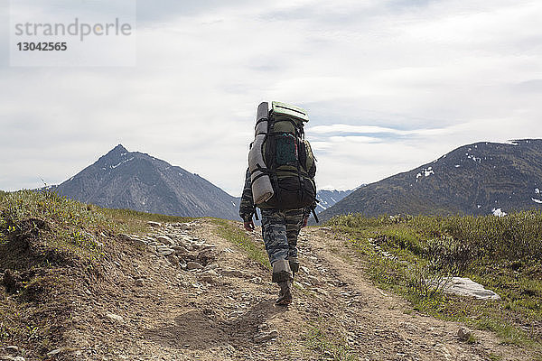 Rückansicht eines männlichen Wanderers mit Rucksack beim Wandern auf einem Berg vor bewölktem Himmel