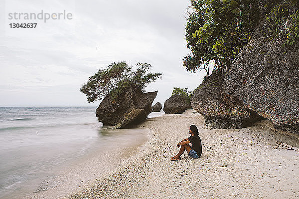 Seitenansicht eines Mannes  der am Strand gegen Felsen sitzt