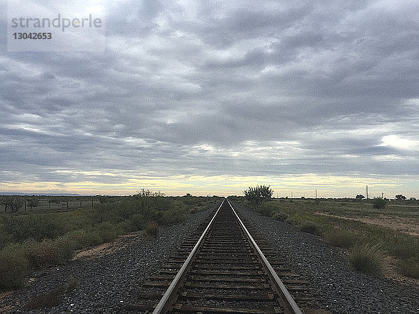 Abnehmende Perspektive der Eisenbahnschiene vor bewölktem Himmel bei Sonnenuntergang