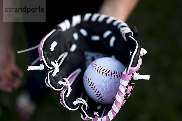 Abgetrennte Hand eines Mädchens  das einen Baseballhandschuh mit Ball trägt