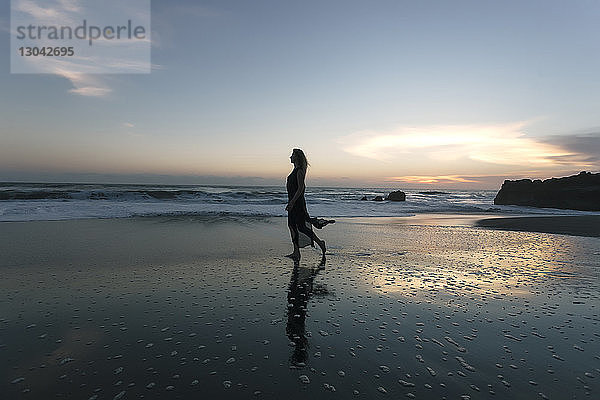 Silhouette einer Frau  die bei Sonnenuntergang am Strand gegen den Himmel läuft