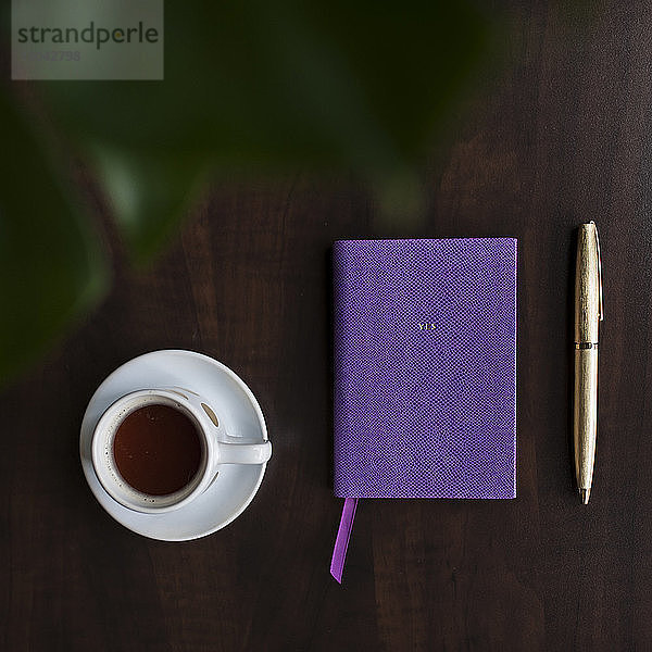 Draufsicht auf Kaffee in der Tasse und Tagebuch auf dem Tisch