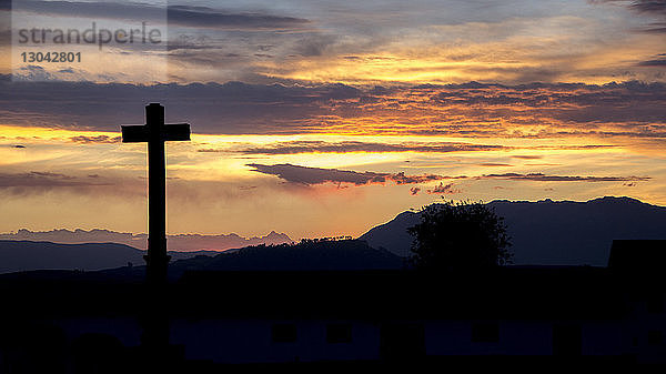 Silhouettenkreuz vor bewölktem Himmel bei Sonnenuntergang