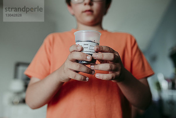 Mittelwert eines Jungen  der zu Hause Erde in einem Einwegbecher hält