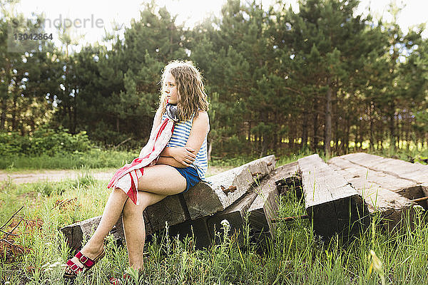 Nachdenkliches Mädchen mit verschränkten Armen auf Holz sitzend auf grasbewachsenem Feld