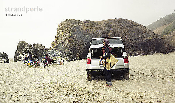 Seitenansicht einer Frau  die am Strand mit dem Auto eine Tasche trägt