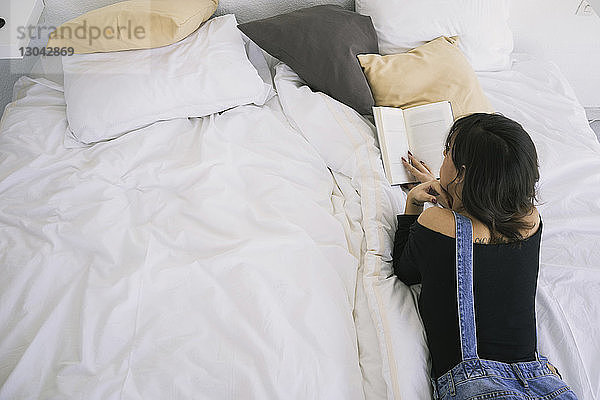 Hochwinkelansicht einer jungen Frau  die zu Hause auf dem Bett liegend ein Buch liest