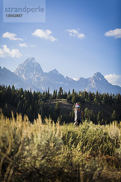 Mann streckt die Arme aus  während er im Bridger-Teton National Forest Yoga auf einem Feld gegen Berge praktiziert