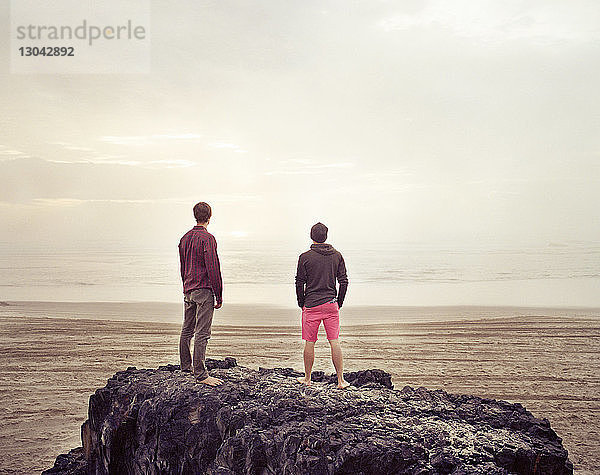 Freunde stehen auf Felsen im Meer gegen den Himmel