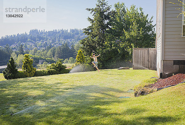 Fröhlicher Junge ohne Hemd spielt auf Grasfeld gegen den Himmel im Hinterhof
