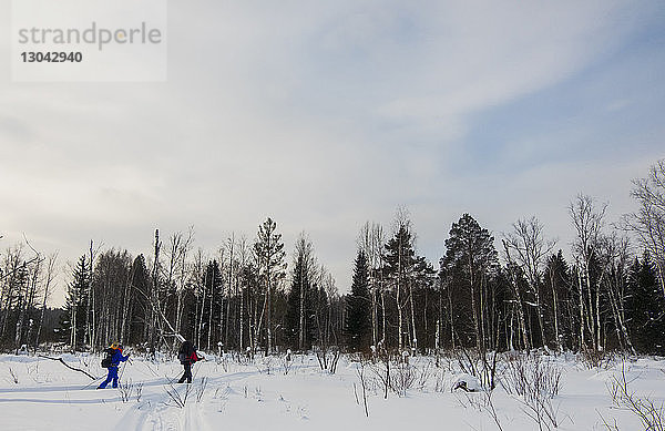 Männliche Freunde wandern auf schneebedecktem Feld gegen wolkigen Himmel