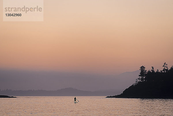 Silhouette einer Person beim Paddelbootfahren auf einem See