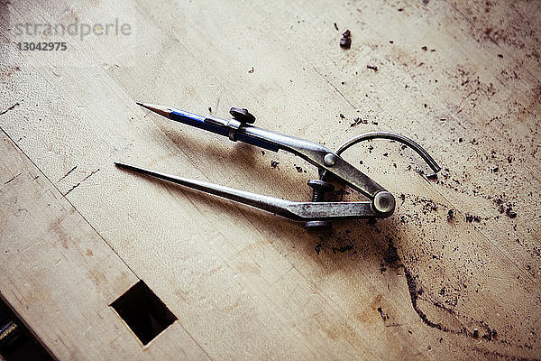 Hochwinkelansicht des Kompasses mit Bleistift auf Holztisch in der Werkstatt
