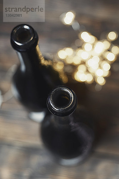 Hochwinkelansicht von Champagnerflaschen mit beleuchteten Weihnachtslichtern auf Holztisch