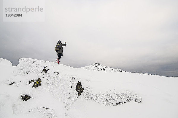 Tiefwinkelansicht eines Wanderers  der auf einem schneebedeckten Feld vor bewölktem Himmel steht