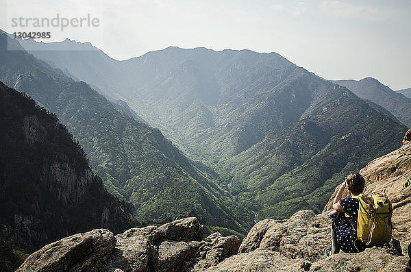 Rückansicht eines Wanderers  der auf Felsen gegen Berge sitzt