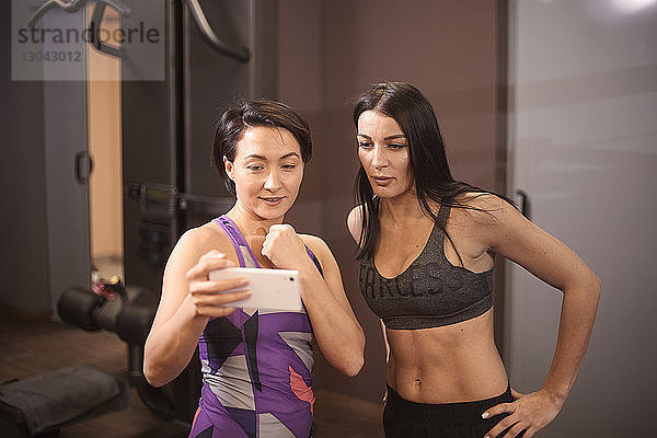 Frau zeigt einem Freund im Fitnessstudio ein Smartphone