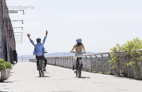 Rückansicht eines Fahrrad fahrenden Paares auf der Promenade an einem sonnigen Tag