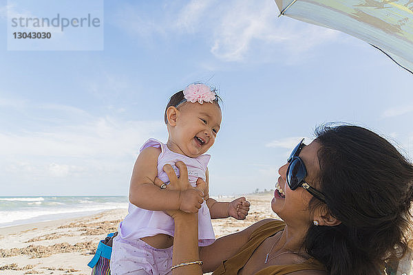 Glückliche Mutter spielt mit Tochter am Strand gegen den Himmel