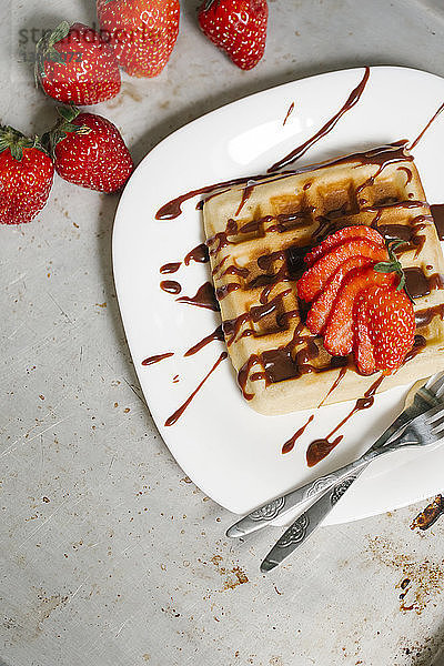 Hochwinkelansicht einer Waffel mit Schokoladensauce und Erdbeerscheiben im Teller auf dem Tisch