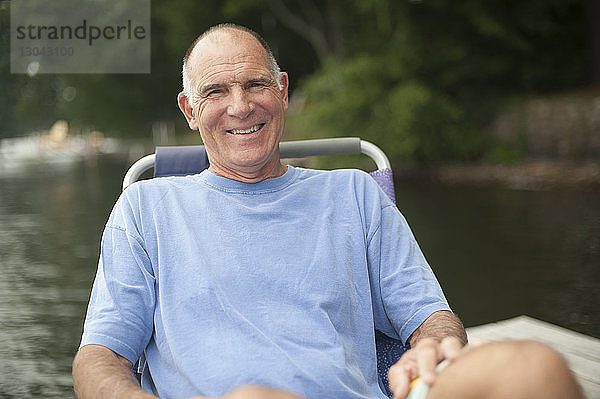 Porträt eines glücklichen Mannes  der sich auf einem Liegestuhl am See entspannt