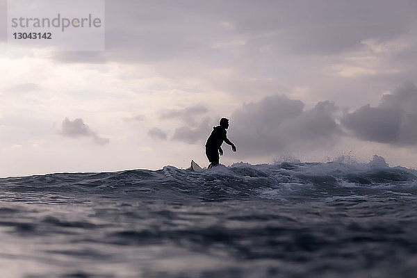 Silhouette eines Mannes  der im Meer vor bewölktem Himmel surft