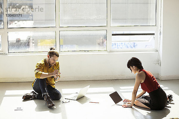 Hochwinkelansicht von Geschäftsleuten  die Laptops am Boden im Kreativbüro benutzen