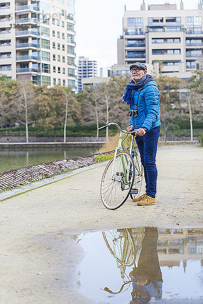Seitenansicht eines Mannes mit Fahrrad  der auf einem Fußweg am Park steht