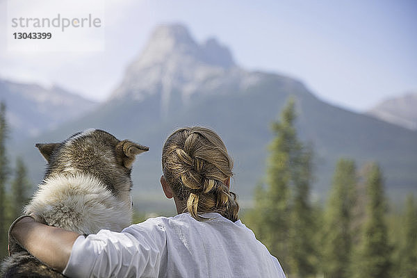 Rückansicht eines Teenager-Mädchens mit Hund beim Sitzen im Banff-Nationalpark