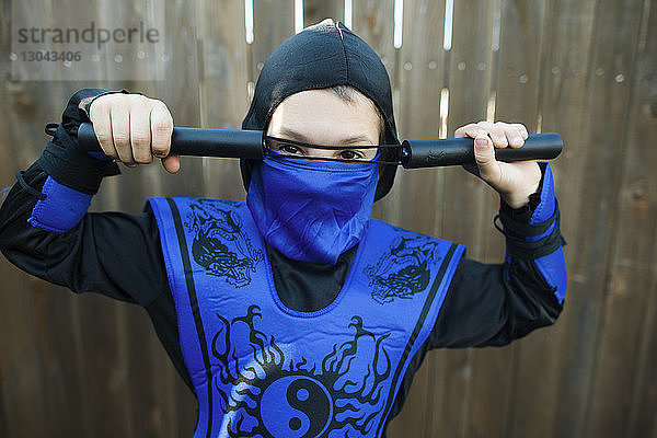 Porträt eines Jungen im Ninja-Kostüm  der an einem Holzzaun steht