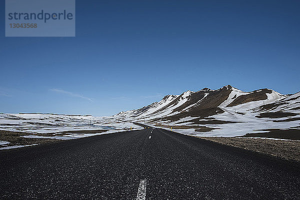 Leere Landstraße durch schneebedeckte Berge vor strahlend blauem Himmel